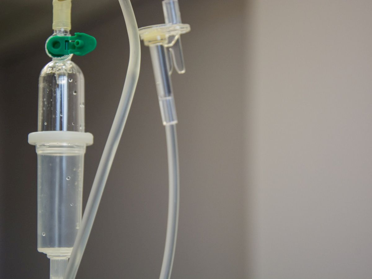 The image shows an intravenous (IV) drip setup with a clear fluid-filled chamber and attached tubes, commonly used in medical settings for fluid administration.