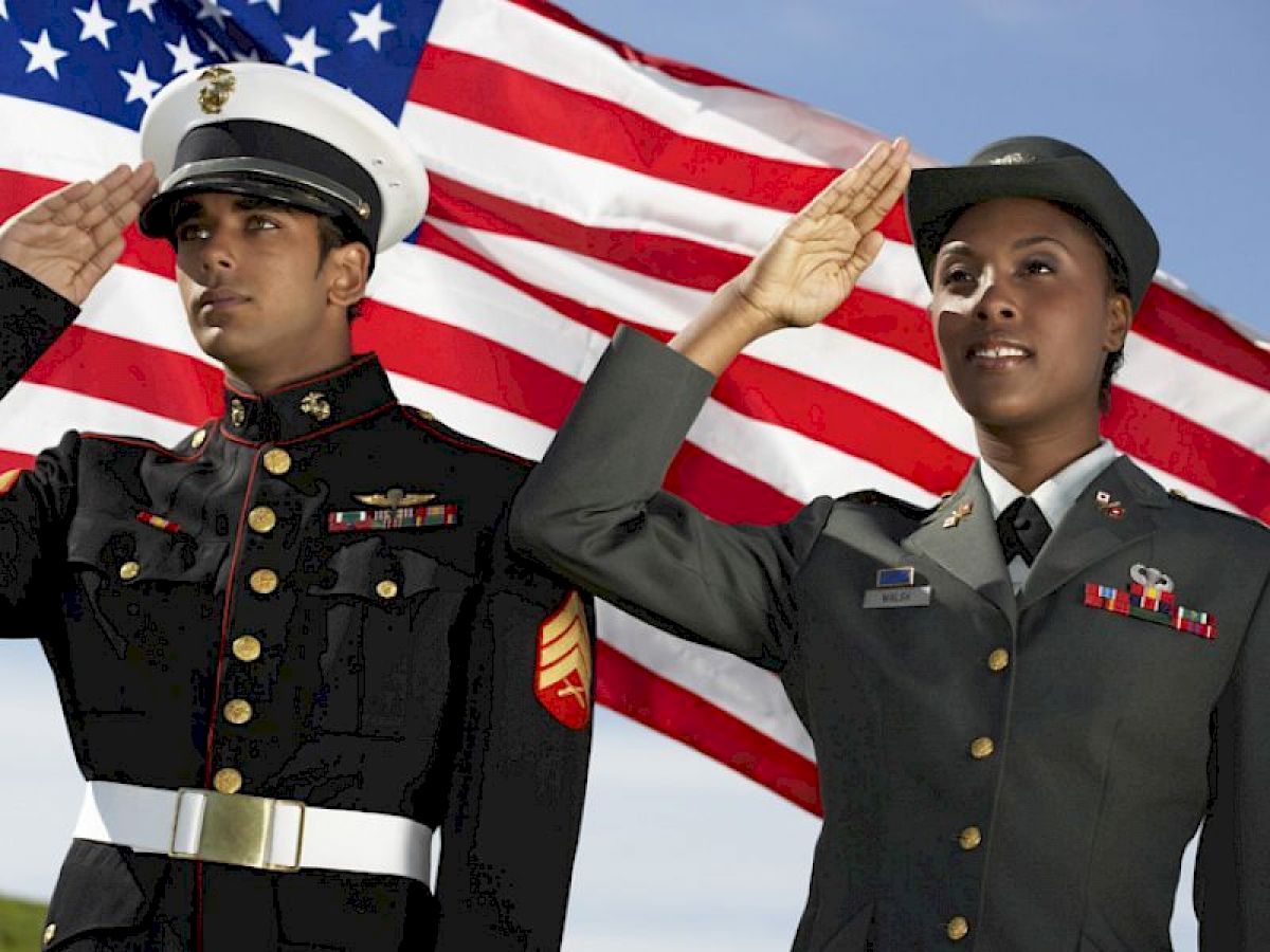 Two military personnel, one male and one female, in uniform saluting in front of an American flag.
