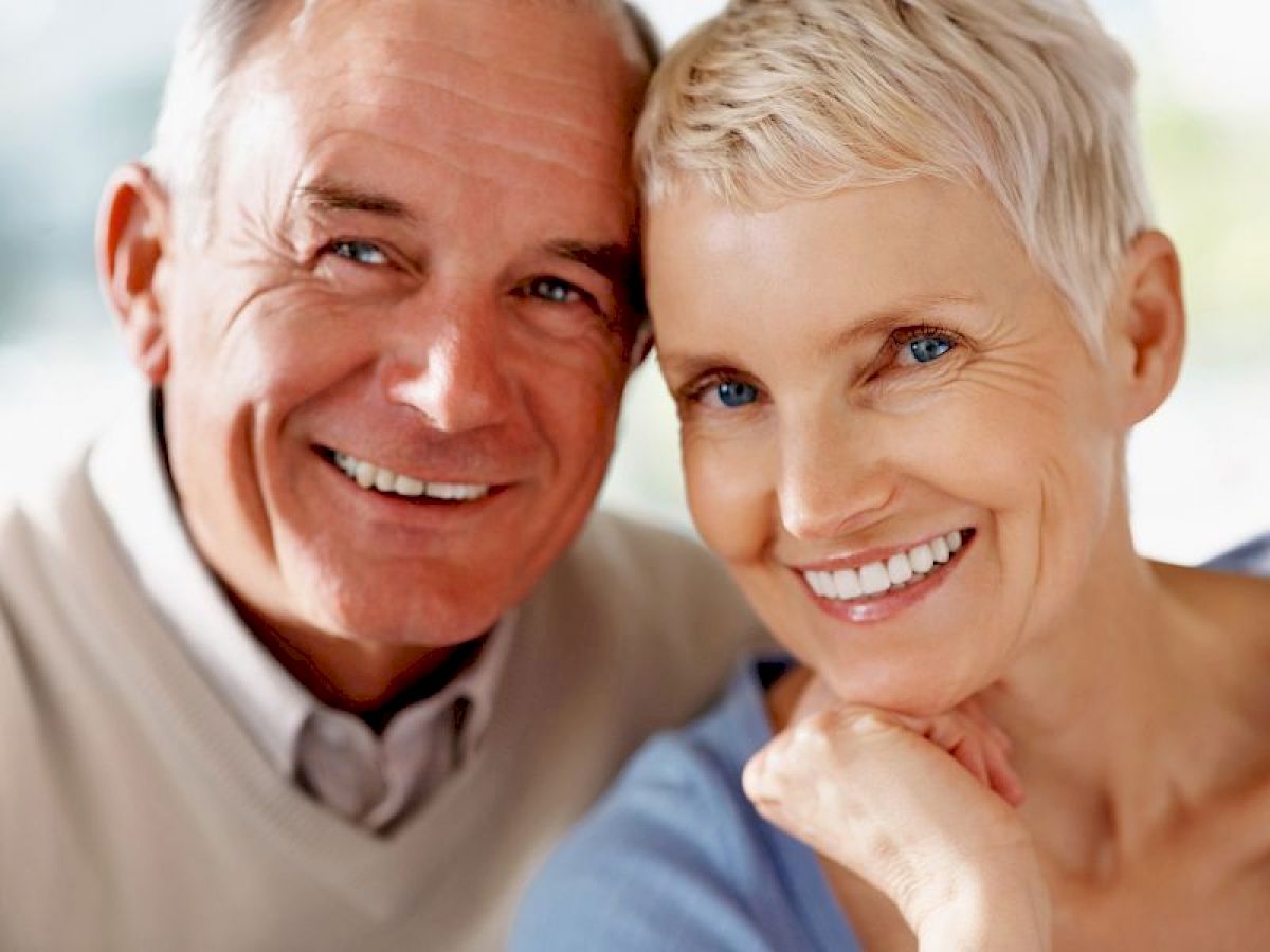 An elderly couple is smiling warmly at the camera, conveying a sense of happiness and companionship.