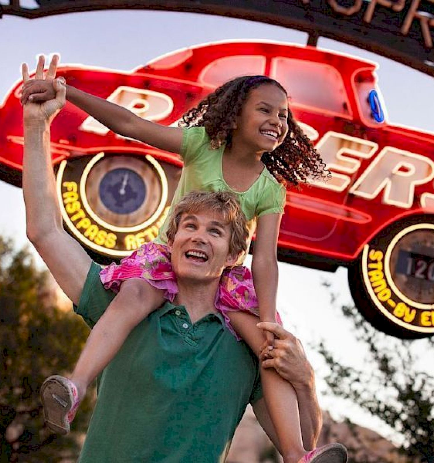A man carrying a girl on his shoulders is smiling in front of a sign with a red car that reads 