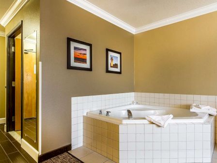 A bathroom corner features a tiled bathtub with white towels and wall art displayed above it. There is also a door and mirror visible.