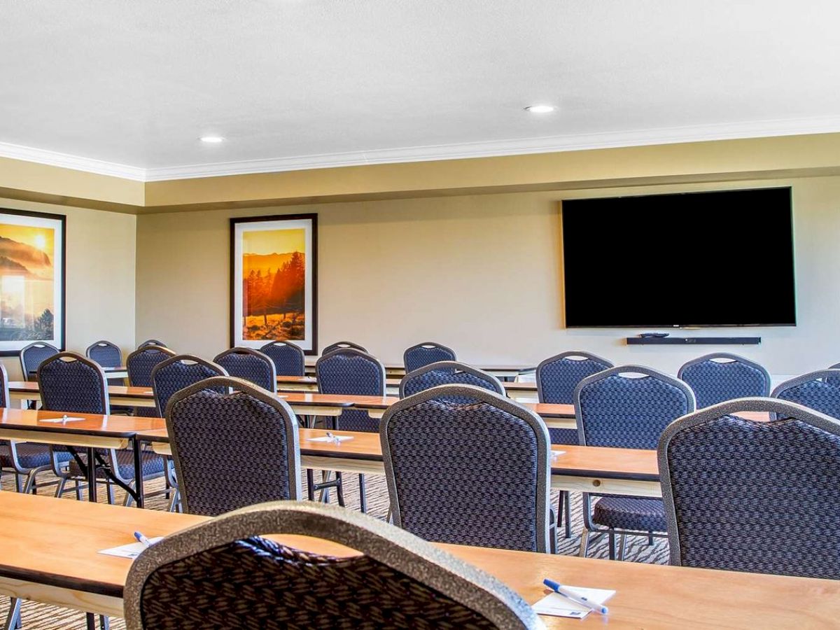 A conference room with rows of chairs and desks, a large wall-mounted TV, and landscape paintings on the walls.