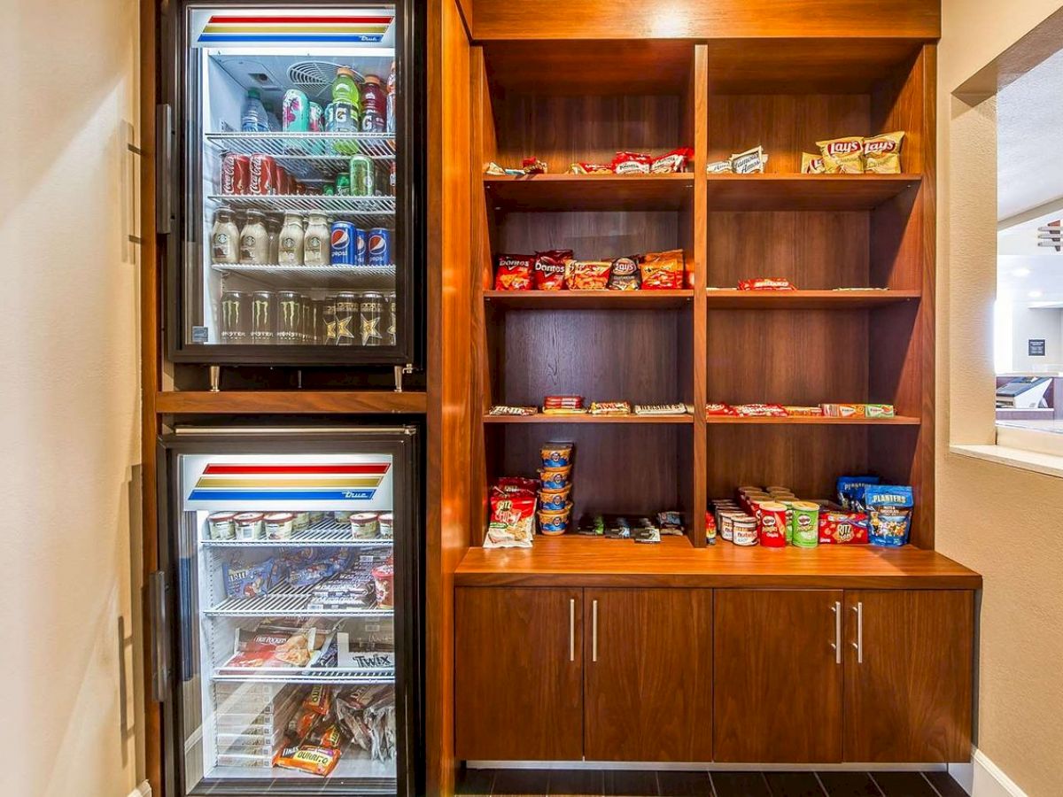 A snack corner with two refrigerators and shelves stocked with beverages, dairy products, snacks, candies, and other packaged items.